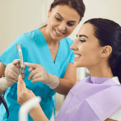 A woman looking at a mirror a dental assistant is pointing at, representing how to maintain dental restorations
