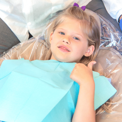 A girl lying on a dentist chair, giving thumbs up, representing foods for strong teeth and gums